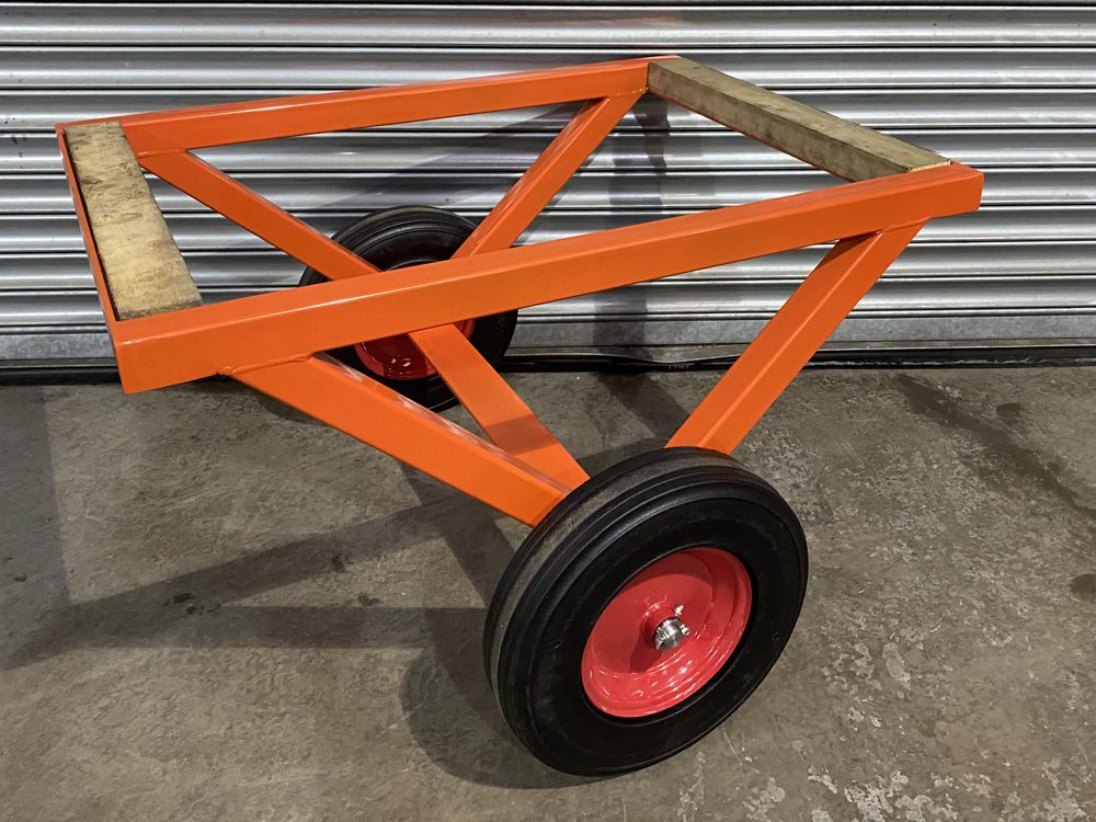 Steel bogey with timber bearers at each end of the top frame and two wheels on red rims